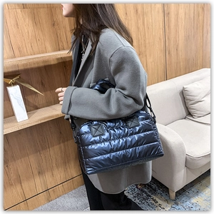Close-up of a blue quilted puffer tote bag styled with a grey coat in a home setting