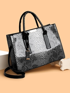 Detail van de tote bag met slangenprint en zwart laklederen handvatten op stenen blok
