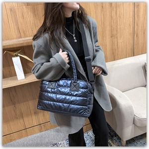 Detail of metallic navy quilted tote bag with black strap in a cozy interior setting