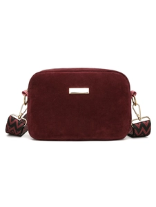 Detail of burgundy suede camera bag featuring golden logo plate and geometric wide strap