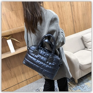 Quilted black puffer tote bag with adjustable strap worn by model in minimalist room
