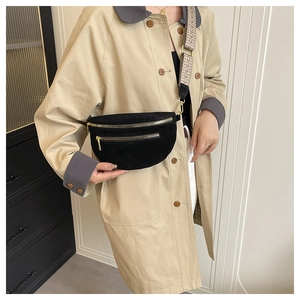 Detail of black suede saddle bag featuring golden zippers and jacquard shoulder strap