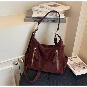 Detail of dark red suede tote bag with golden zippers and adjustable straps on a bench