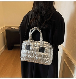 Silver quilted duffel bag with black straps worn by a model in a warm indoor setting