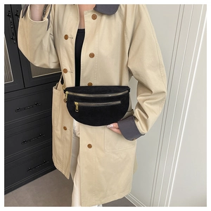 Fashionable black suede crescent bag with dual gold zippers worn over a khaki trench coat