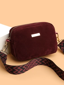 Detail of burgundy suede crossbody bag with golden hardware and colorful woven strap