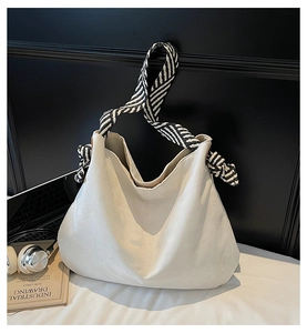 Detail of minimalist cream white large hobo bag with striped strap and knot accents