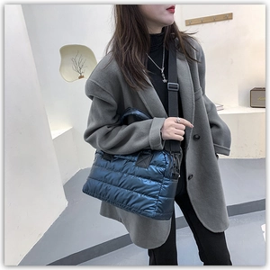 Detail of navy quilted puffer tote bag with adjustable strap worn by model in grey coat