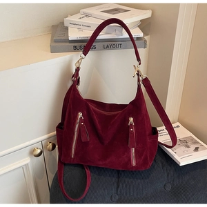 Detail of burgundy suede tote bag featuring dual front zippers and polished gold hardware