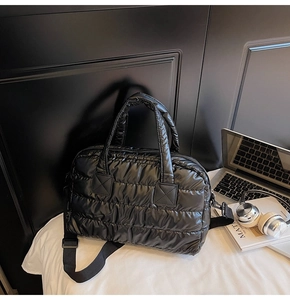 Close-up of black quilted puffer bag with silver laptop and headphones on a desk