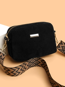 Detail of black suede camera bag with geometric pattern wide strap and gold hardware