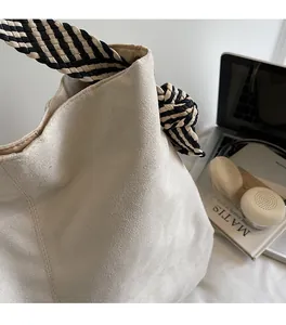Detail of off-white suede tote bag featuring a black and white woven knotted strap