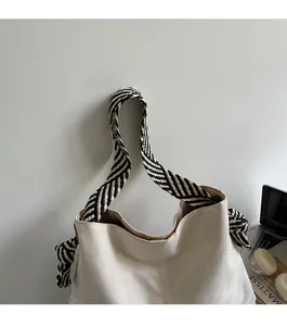 Close-up of beige suede tote bag featuring a decorative black and white woven wide strap