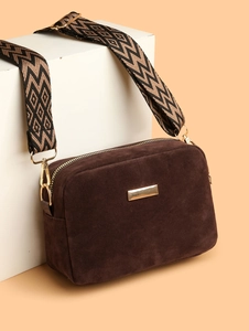 Close-up of brown suede camera bag with wide geometric woven strap and gold hardware