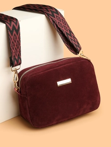 Detail of burgundy suede camera bag with geometric patterned woven shoulder strap