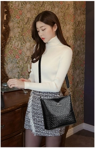 Detail of black woven texture bucket bag with gold logo on white knitwear outfit