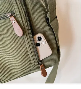 Détail du sac à bandoulière en velours côtelé vert avec poche zippée et smartphone