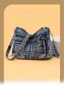 Detail shot of blue washed denim crossbody bag featuring multiple zipper pockets and logo