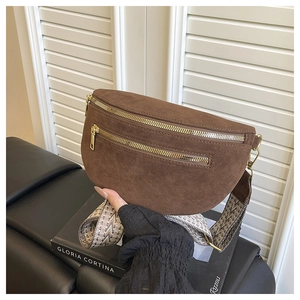 Close-up of brown suede saddle bag featuring dual gold zippers and ethnic woven strap