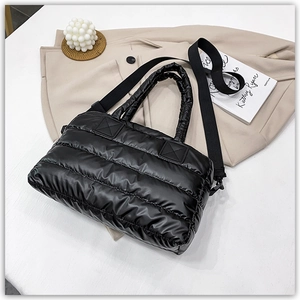 Detail of black quilted puffer tote bag with adjustable shoulder strap on beige fabric
