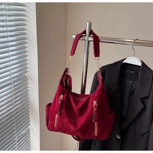 Detail of burgundy suede tote bag featuring vertical zippers and wide shoulder strap