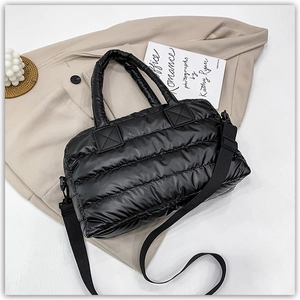 Flat lay of black puffer tote bag with quilted texture and adjustable shoulder strap