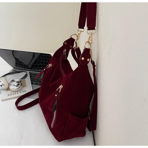 Close-up of burgundy suede tote bag featuring golden zippers and multi-strap design