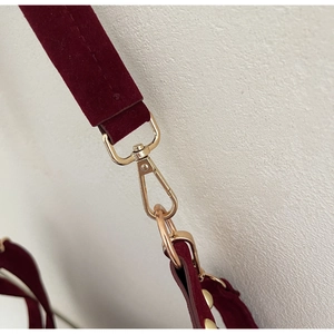Detail of burgundy velvet shoulder strap with gold metal buckle on a tote bag