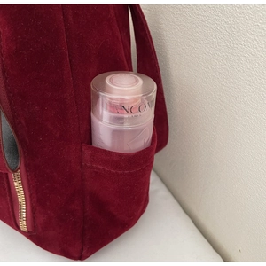 Detail of the side pocket on a dark red velvet backpack showing storage for skincare items