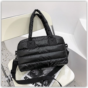 Detail of black puffer tote with quilted texture and adjustable shoulder strap on a chair