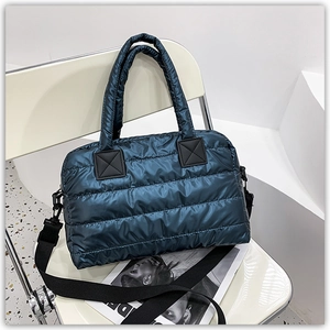 Detail of teal quilted tote bag with wide nylon strap on a minimalist white chair