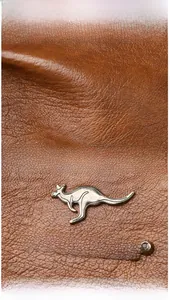Detail shot of brown lychee grain leather with silver kangaroo metal logo and brand lettering