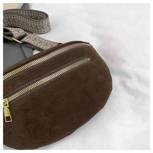 Detail of dark brown suede chest bag with golden zippers and chevron textured strap
