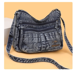 Detail of blue denim crossbody bag featuring multi-layer zippers and kangaroo metal logo