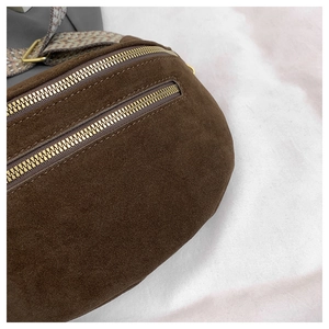 Close-up of dark brown suede fanny pack with gold zippers and geometric strap