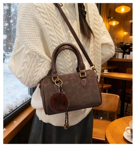 Détail du sac Boston marron foncé en daim avec ferrures dorées et pompon décoratif