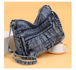 Detail view of washed blue denim crossbody bag featuring multiple zipper pockets and logo