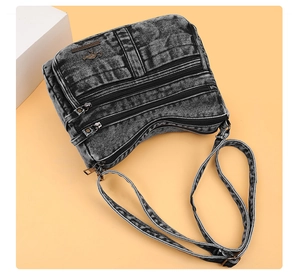 Detail of washed denim crossbody bag featuring triple zippers and kangaroo metal logo