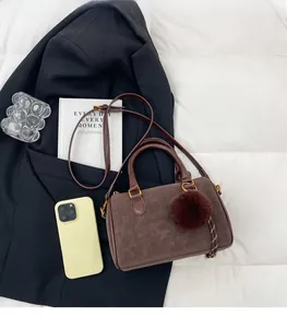 Sac Boston marron avec breloque peluche et sangle tissée sur un manteau noir élégant