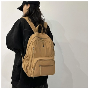 Side view of a brown multi-pocket nylon backpack worn by a model in casual streetwear style