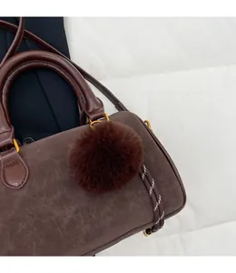Détail du sac Boston marron foncé avec pompon en fausse fourrure et finitions dorées
