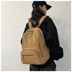 Rear view of khaki nylon travel backpack with multiple pockets on female model