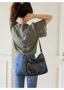 Detail of grey denim crossbody bag with multiple zipper pockets and logo patch