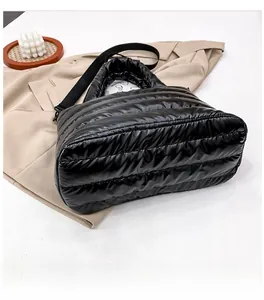 Detalle del bolso acolchado negro brillante con costuras sobre una gabardina beige