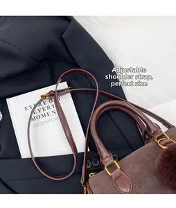 Détail du sac Boston en cuir marron foncé avec pompon en fourrure et finitions dorées