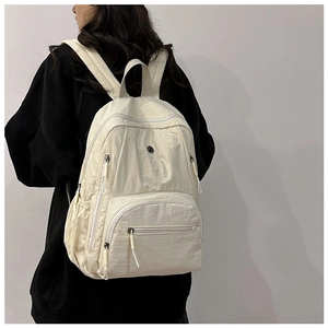 Close-up of cream nylon backpack on model showing multi-pocket design and texture