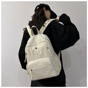 Rear view of a cream white nylon backpack with multiple pockets on a model in black hoodie