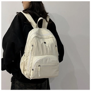 Detail of a cream-white nylon backpack featuring multiple pockets and high-capacity design