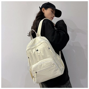 Detail view of cream nylon backpack with multi-pocket design and smooth zippers