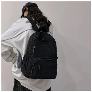 Detail of a lightweight black nylon backpack showing multi-pocket design and side bottle holder